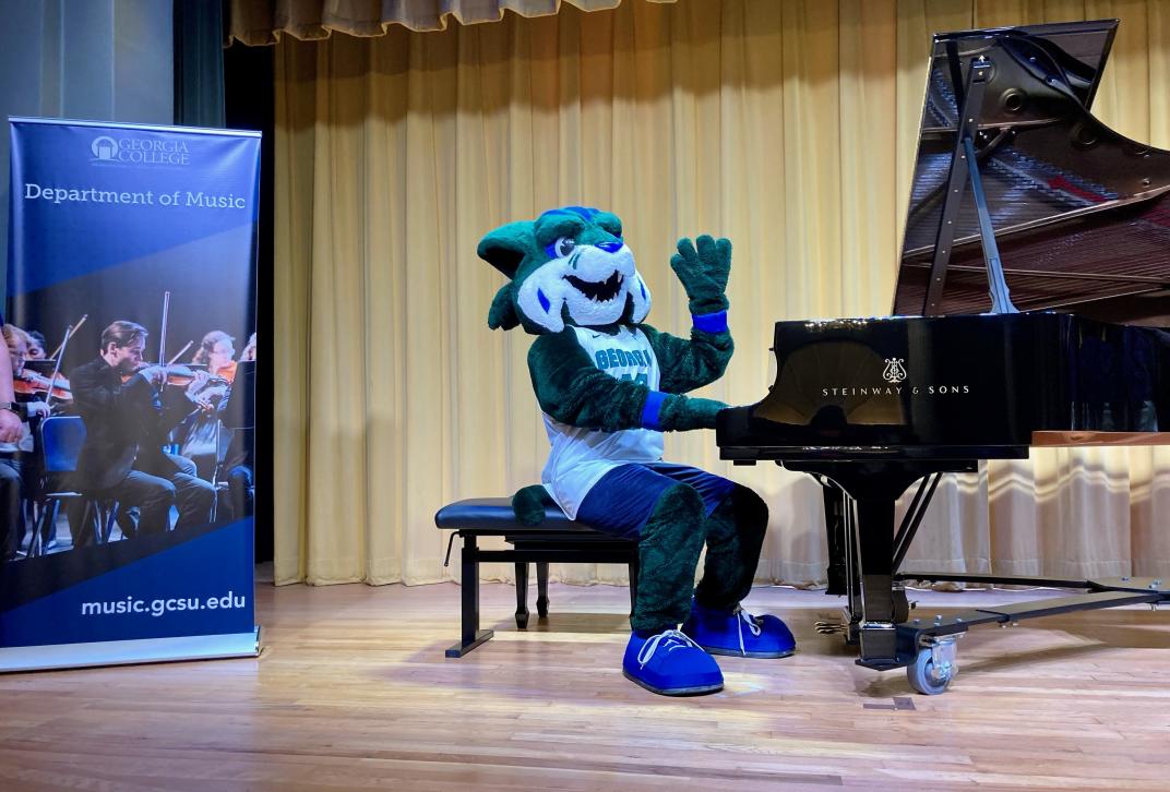 Bobcat mascot sitting on stage at a grand piano