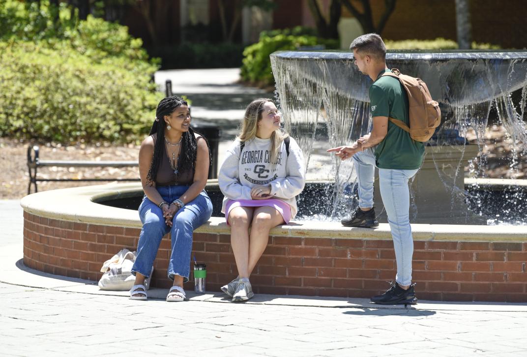 Three students talk at the campus fountain