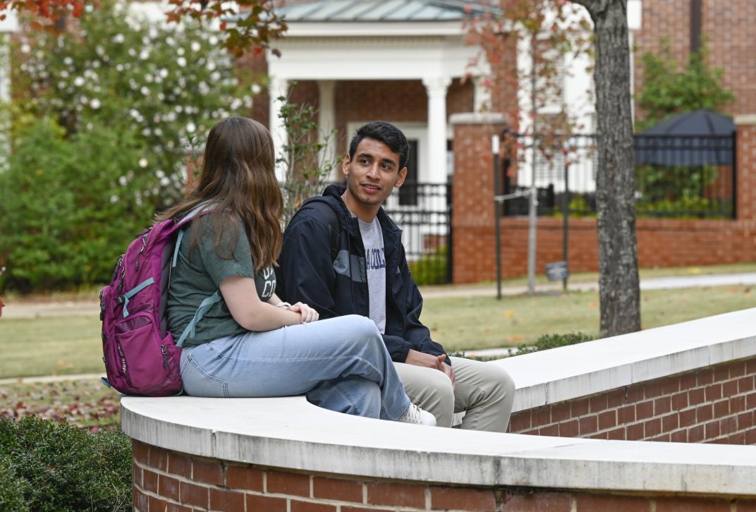 Two students sit on a ledge talking to each other